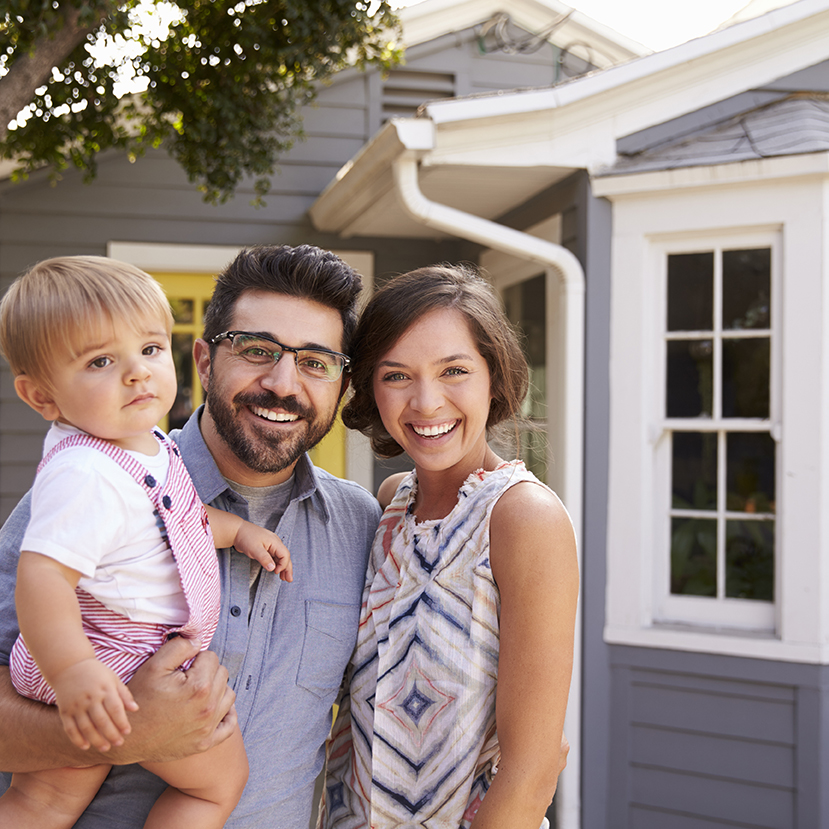 Portrait Of Excited Family Standing Outside New Home